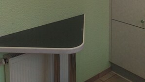 Una cocina con una pared verde, tres cuadros enmarcados, una encimera blanca y un armario.