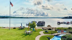 A waterfront property with a flag, a swimming pool, and boats docked in the background.