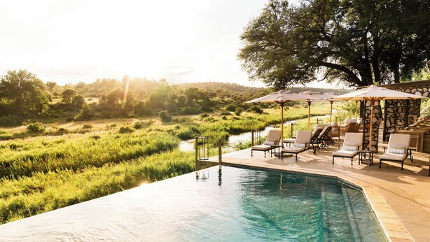Une piscine à débordement bordée de chaises longues et d’ombrelles, entourée d’une végétation luxuriante et offrant une vue imprenable sur le paysage.