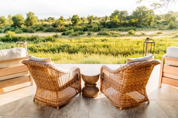 A wicker chair and sofa set on a patio with a view of a grassy field and trees.