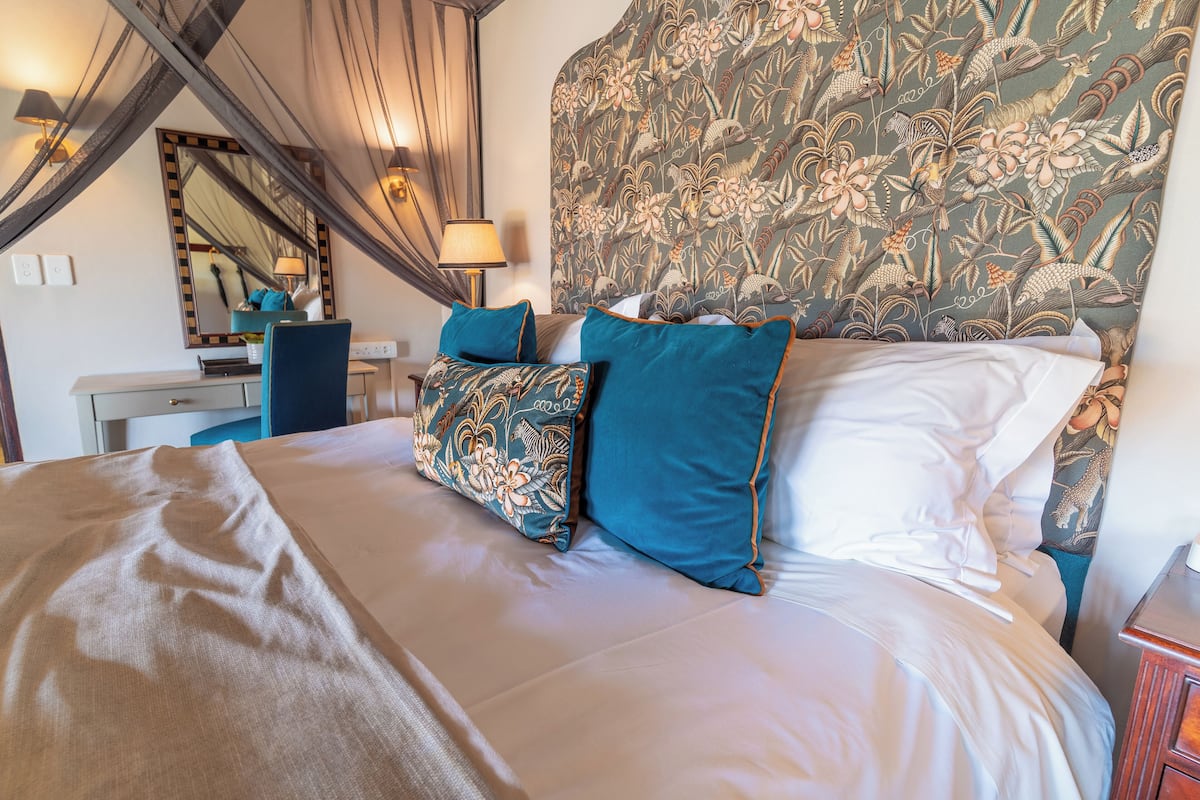 A neatly made bed with a floral headboard, a bedside table with a lamp, and a mirror on the wall.