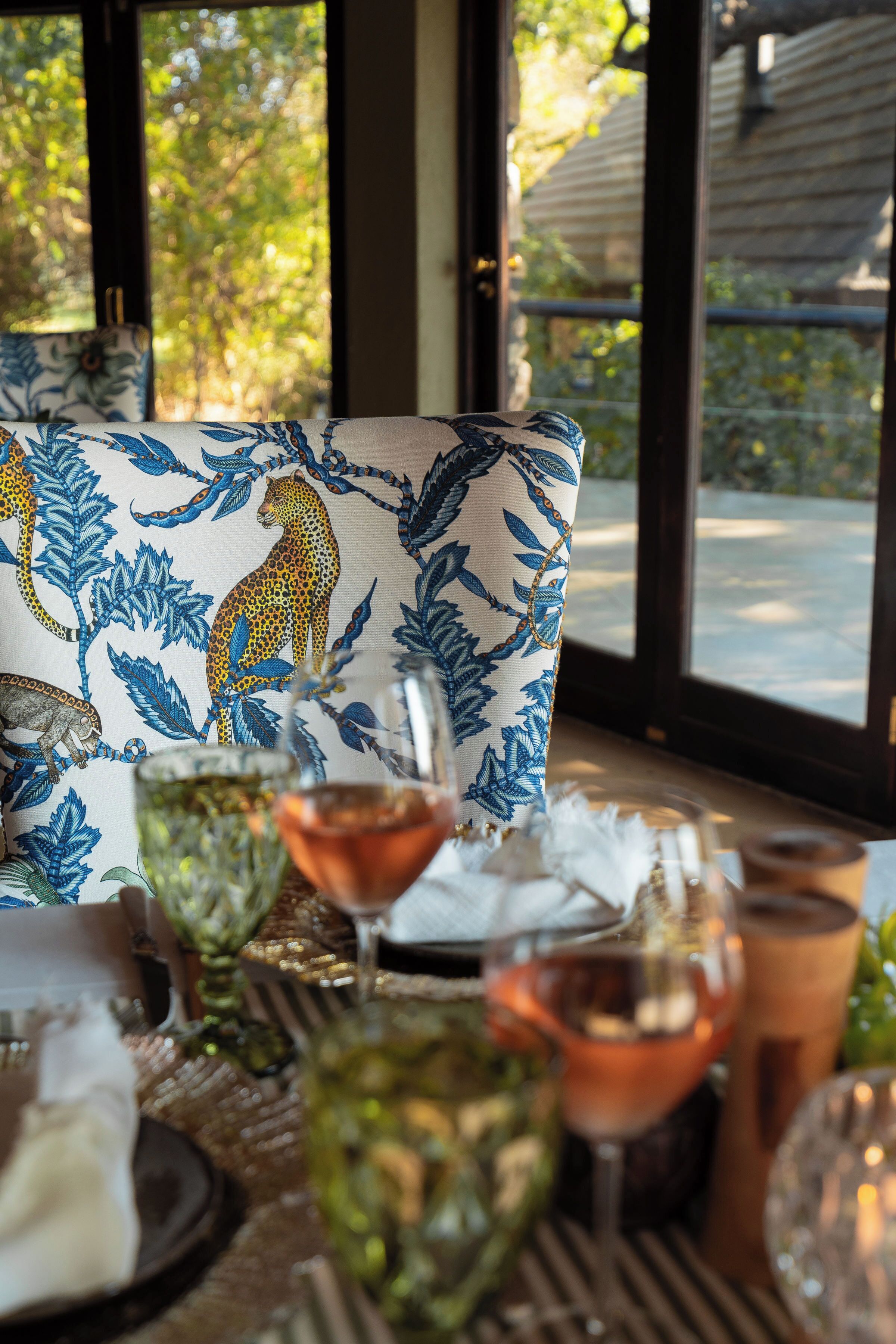 A dining table with a patterned cushion, glassware, and a view of greenery outside.