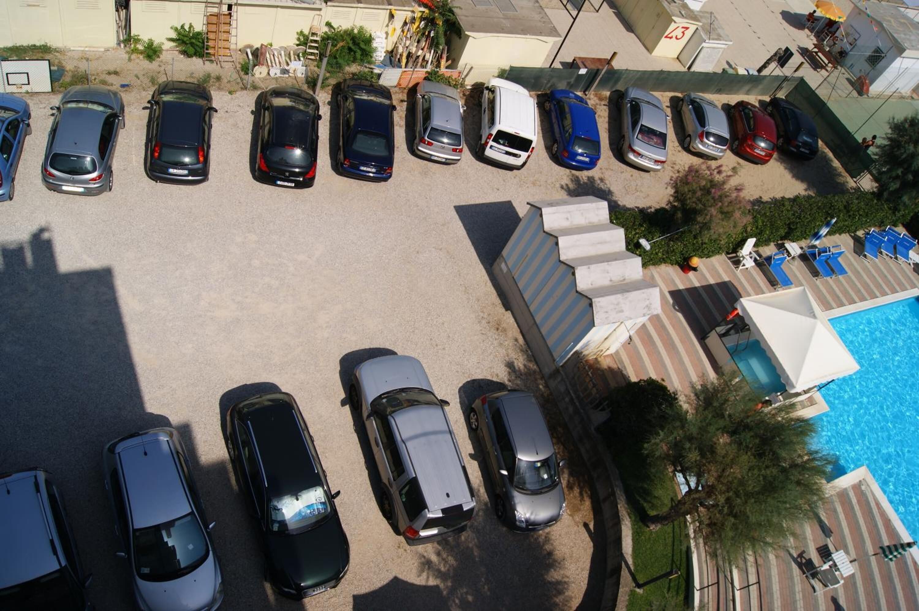 A parking lot with multiple cars and a swimming pool area with lounge chairs.