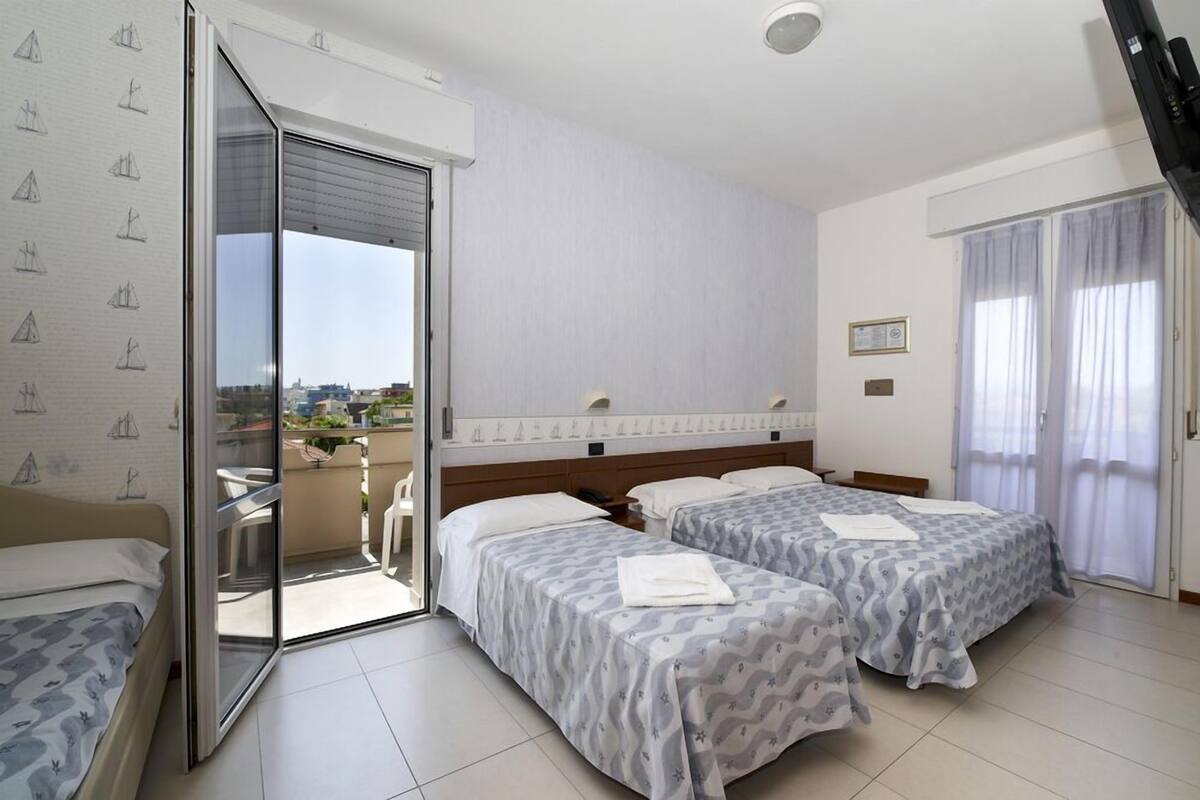 A hotel room with two beds, a sliding glass door to a balcony, and a view of the city.