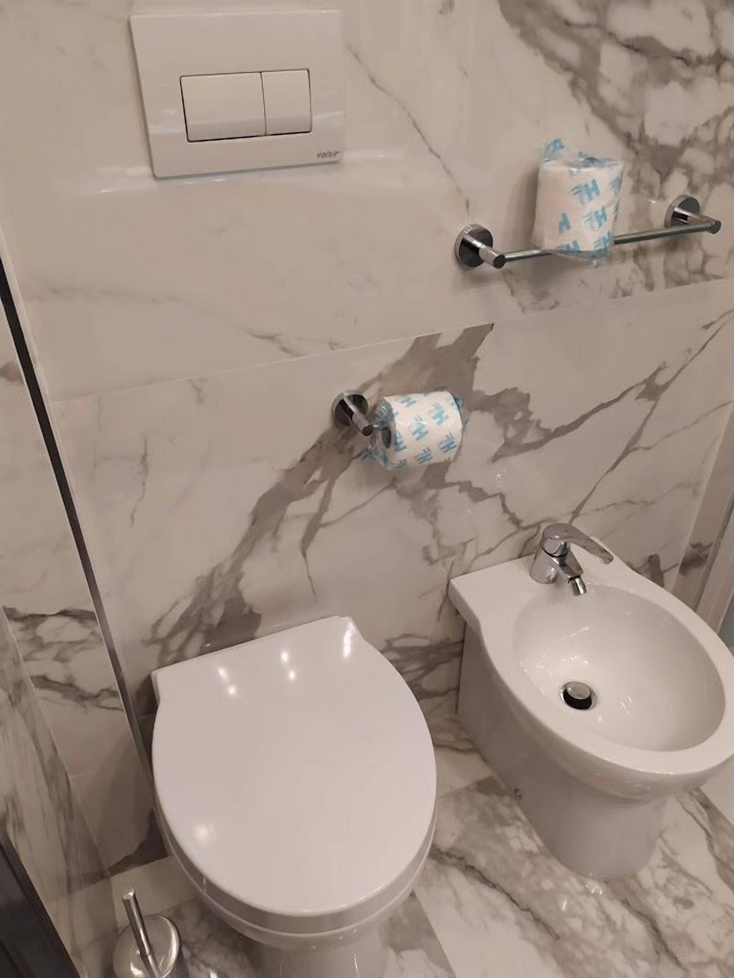 Une salle de bain équipée de toilettes, d’un bidet et d’un mur en marbre.