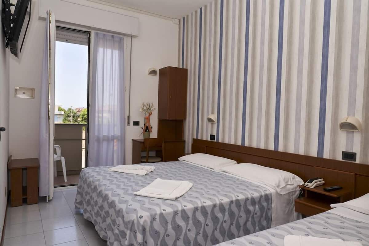 A hotel room with two beds, a wooden wardrobe, a desk, and a chair.