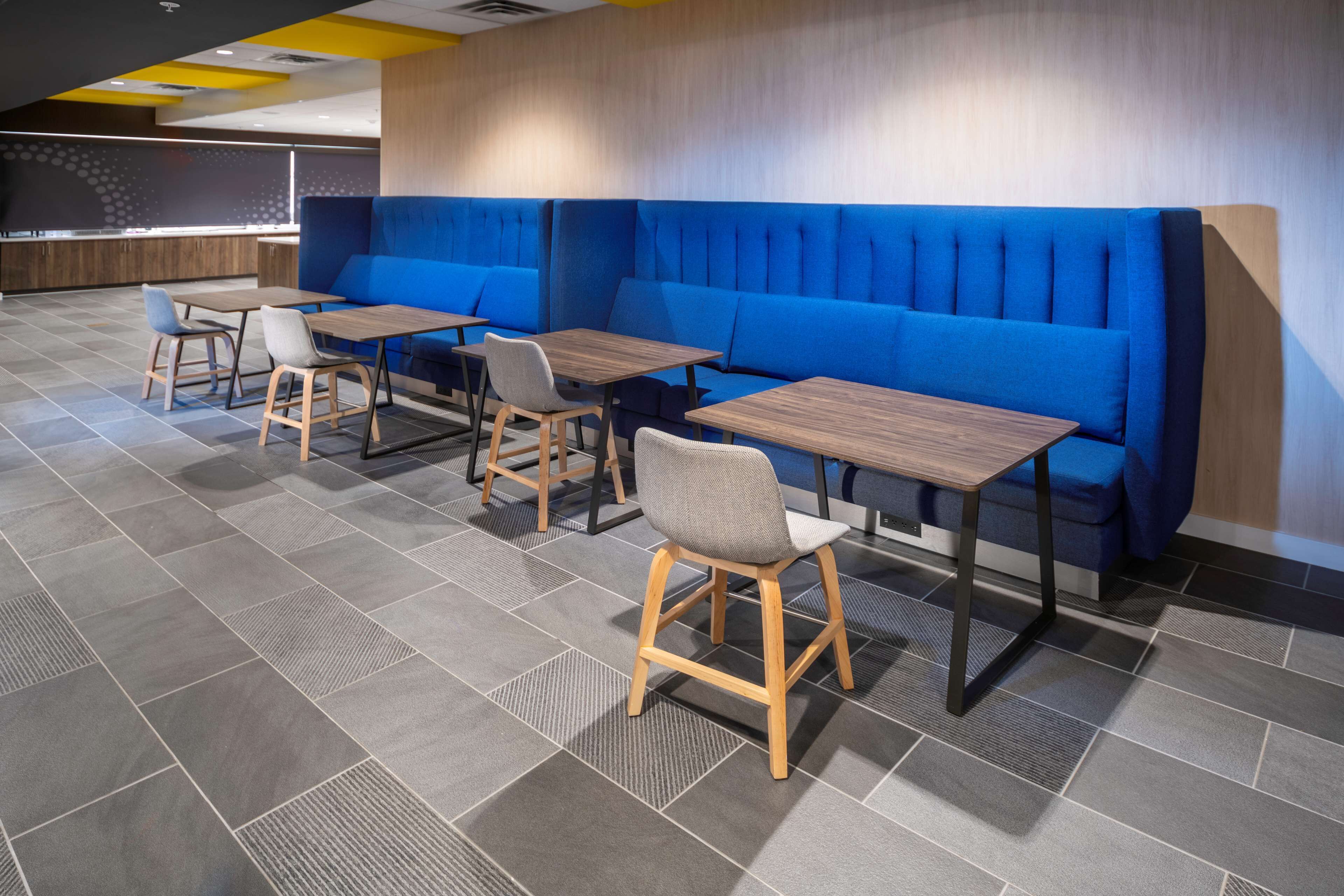 Een modern restaurant met blauwe bankjes, houten tafels en grijze stoelen.