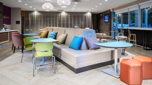A modern lounge area with a sofa, colorful chairs, a round table, and orange ottomans. - Tru by Hilton Minneapolis Mall of America (Bloomington)