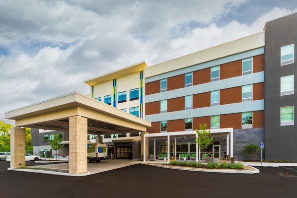 A multi-story hotel with a covered entrance, outdoor seating area, and a parking lot. - Tru by Hilton Minneapolis Mall of America (Bloomington)