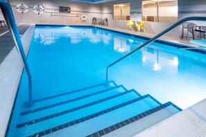 An indoor swimming pool with clear blue water, steps leading into the pool, and a lifeguard station with a sign. - Tru by Hilton Minneapolis Mall of America (Bloomington)