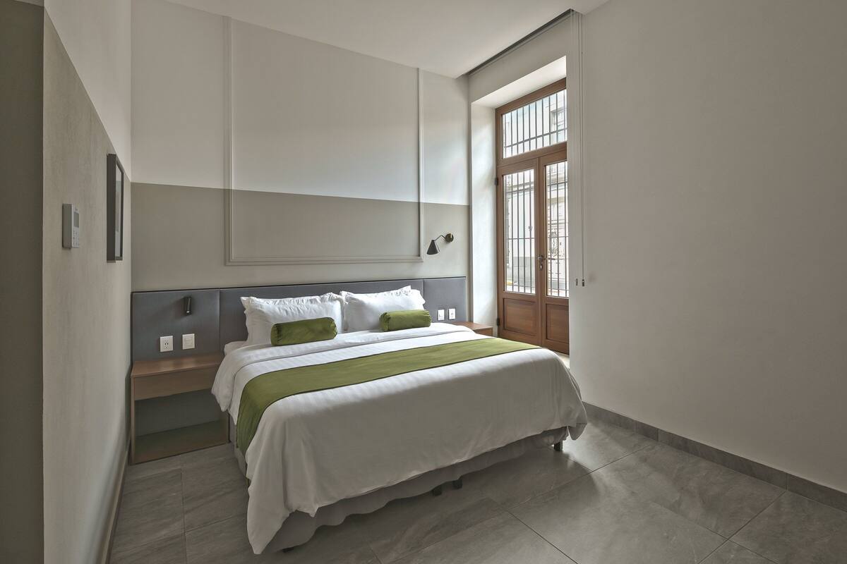 A modern bedroom with a bed, bedside tables, and a large window.