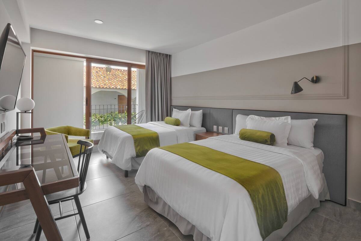 A hotel room with two beds, a desk, and a balcony.
