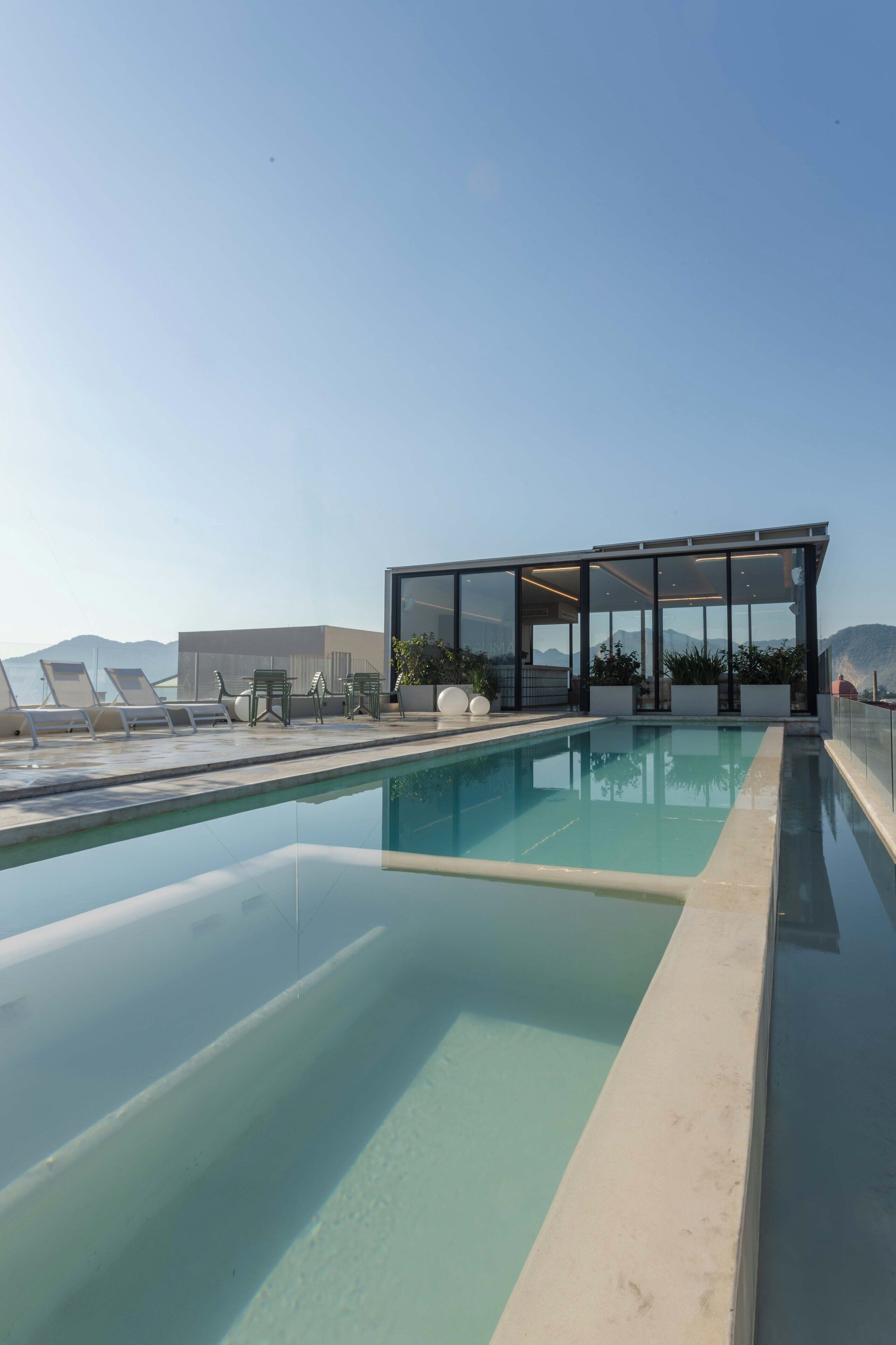 A rooftop pool with lounge chairs and a glass-enclosed structure.