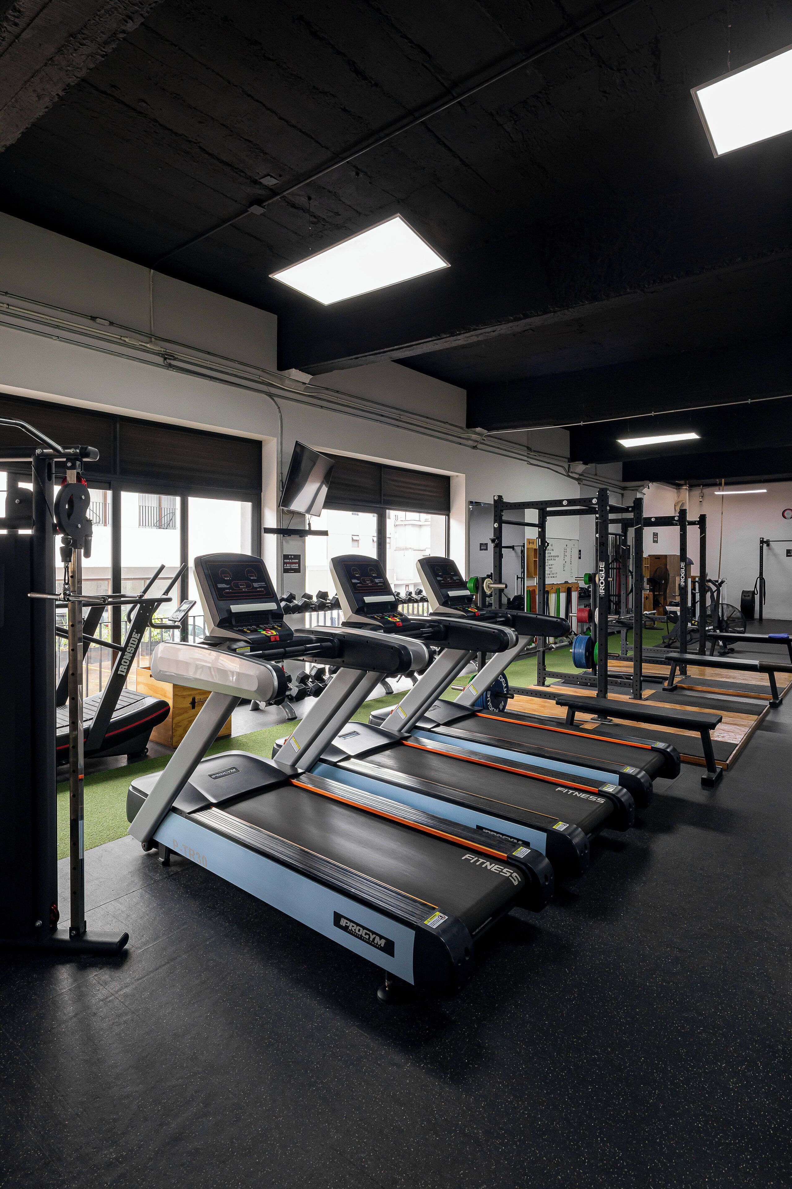Une salle de sport équipée de tapis de course, de machines de musculation et d’un support pour les exercices de squat.