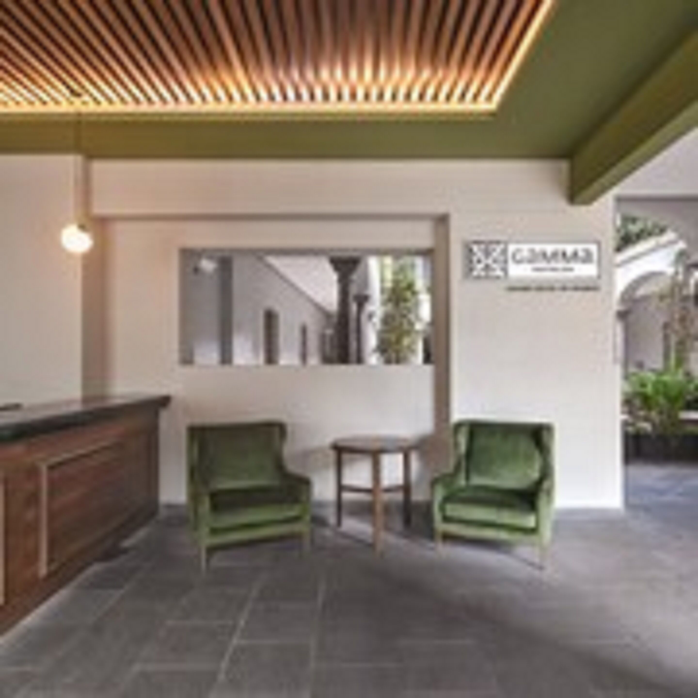 Un área de recepción con techo de madera, un mostrador de recepción, dos sillones verdes y una pequeña mesa.