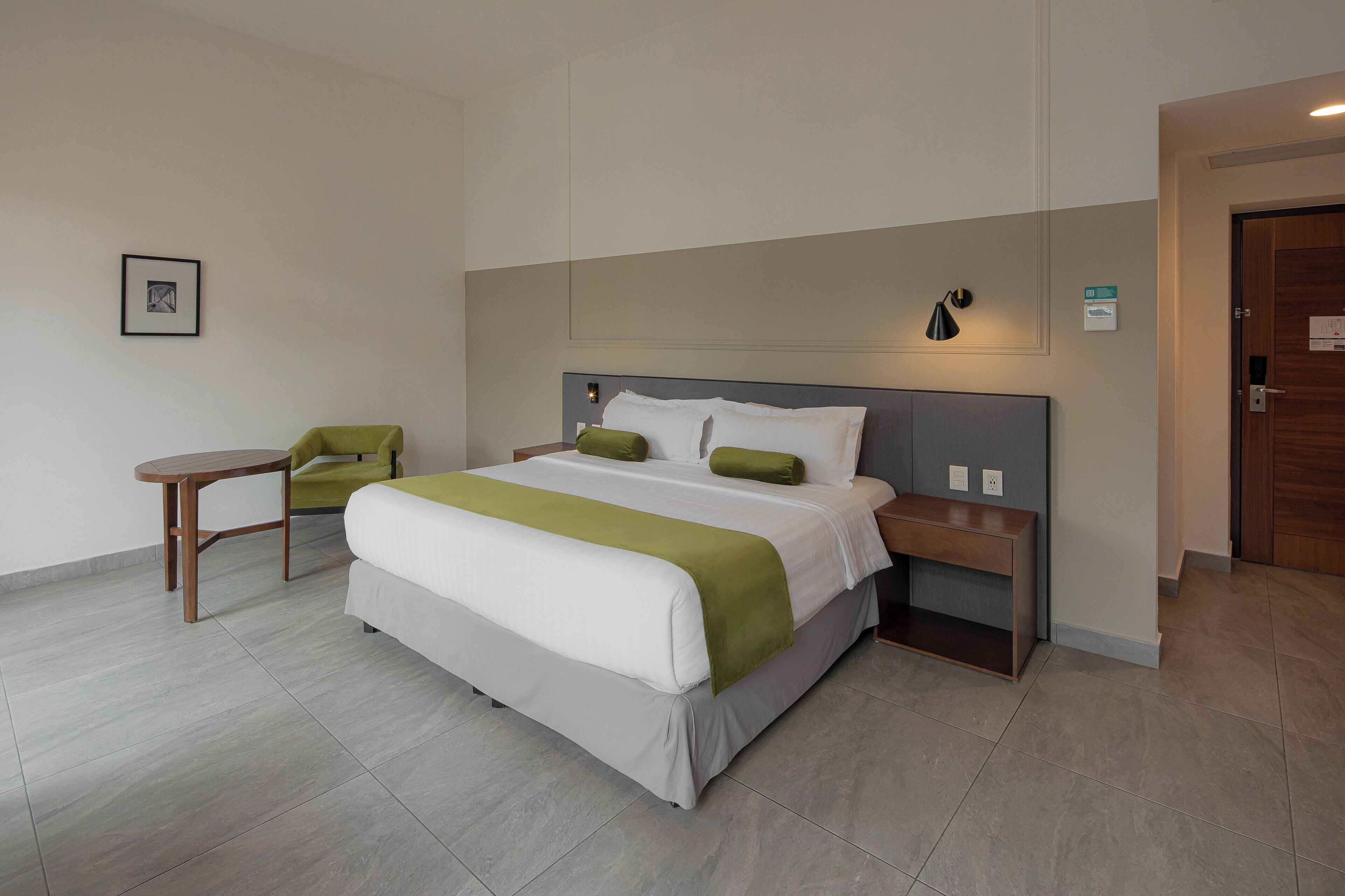 A hotel room with a bed, bedside tables, a chair, and a small table.