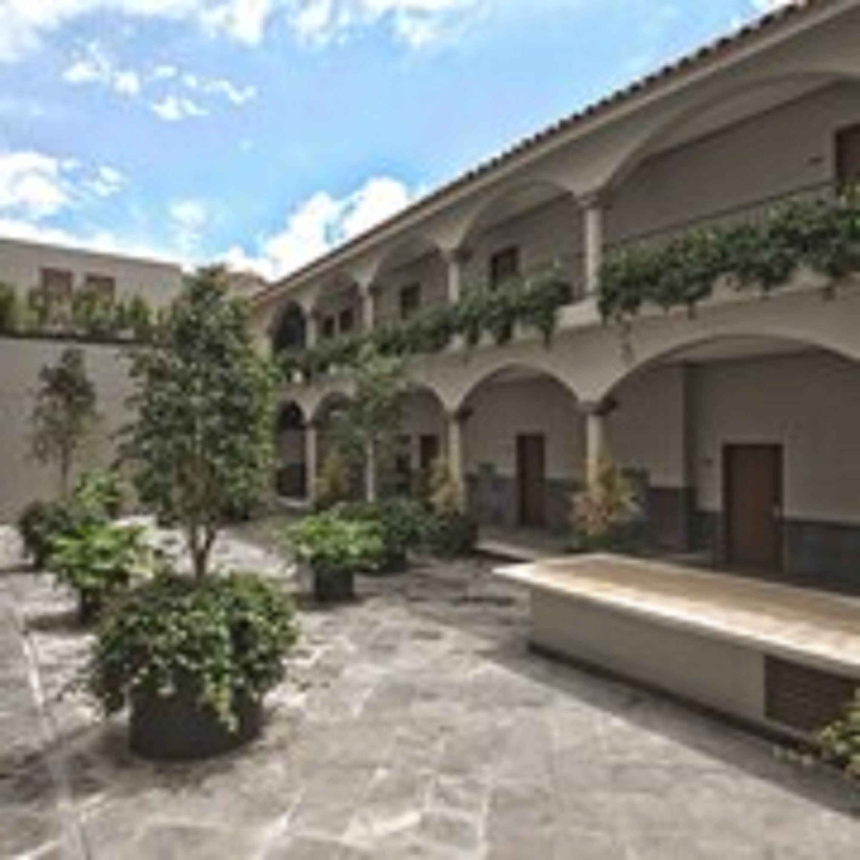 A courtyard with stone flooring, arches, and potted plants.