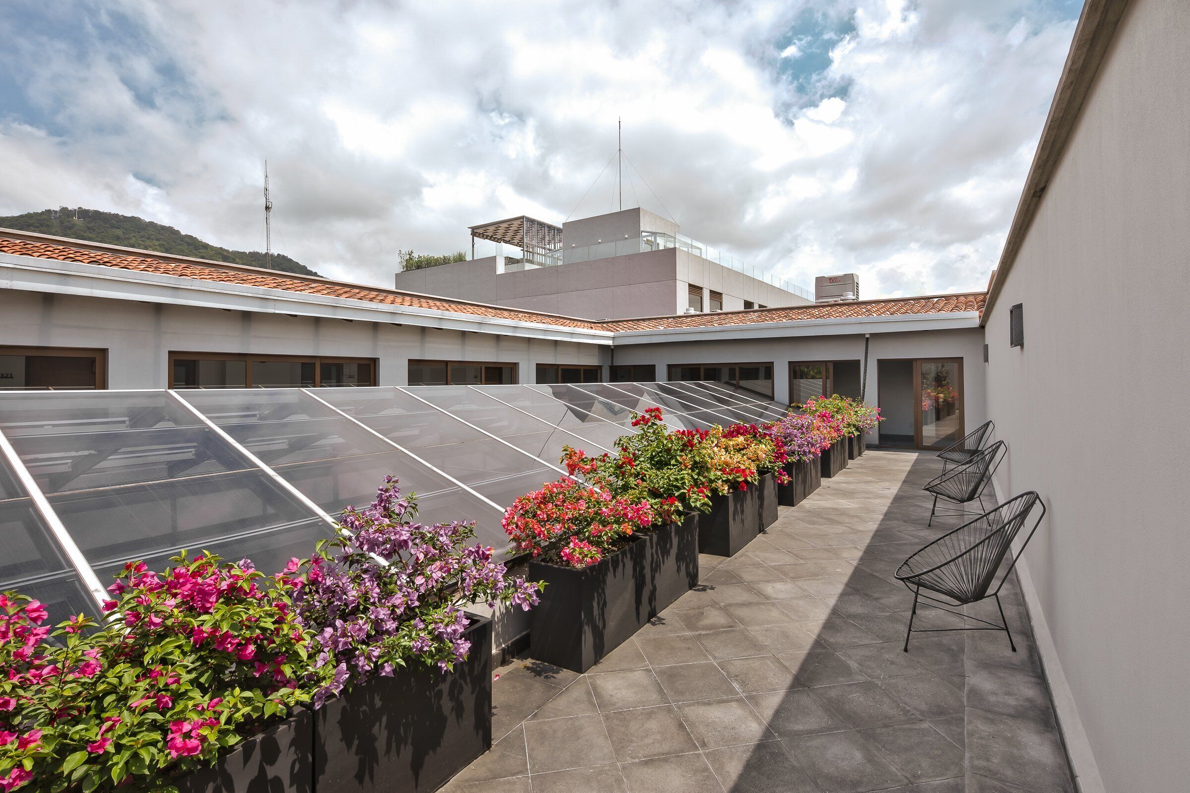 A rooftop terrace with solar panels, flower planters, and seating areas.