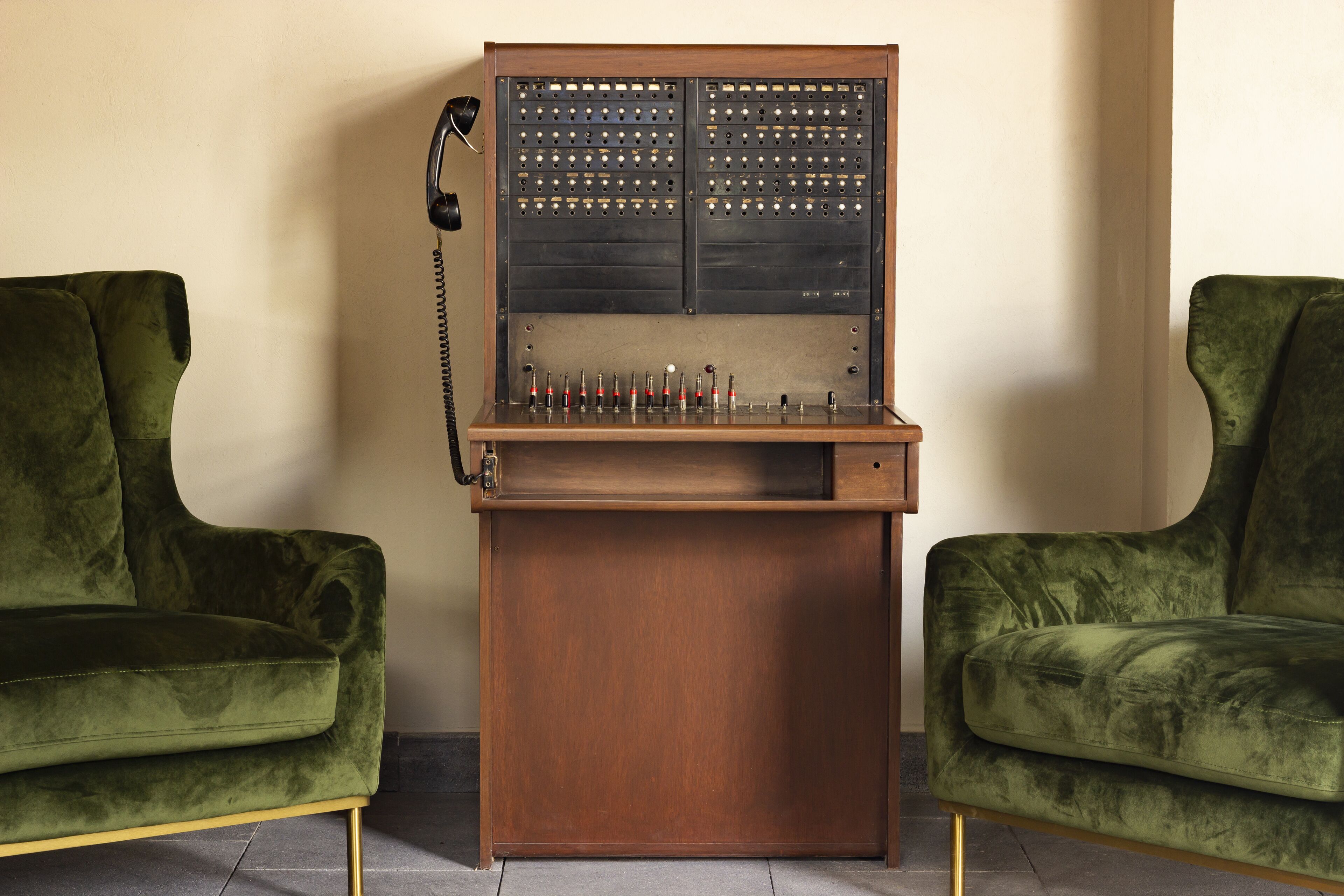 Une cabine téléphonique ancienne, dotée d’une base en bois et d’un panneau métallique percé de plusieurs trous.