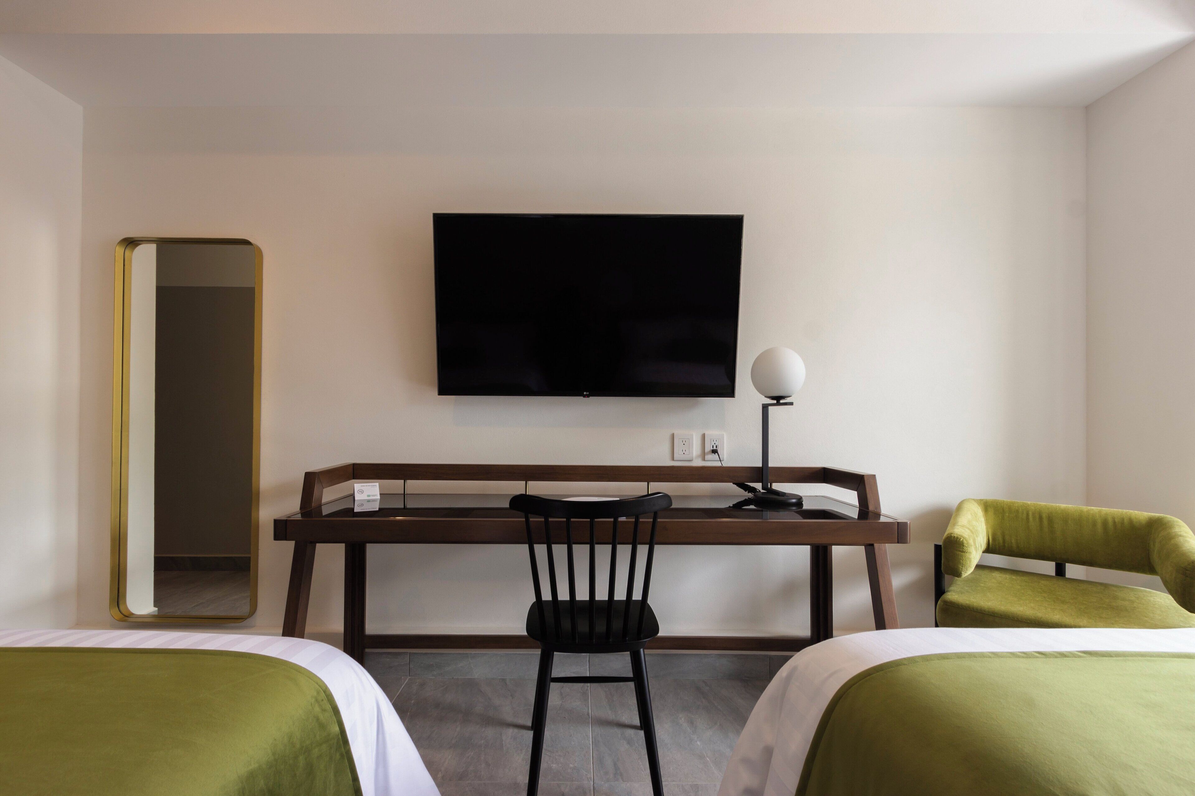 A hotel room with two beds, a desk with a chair, a television, and a mirror.