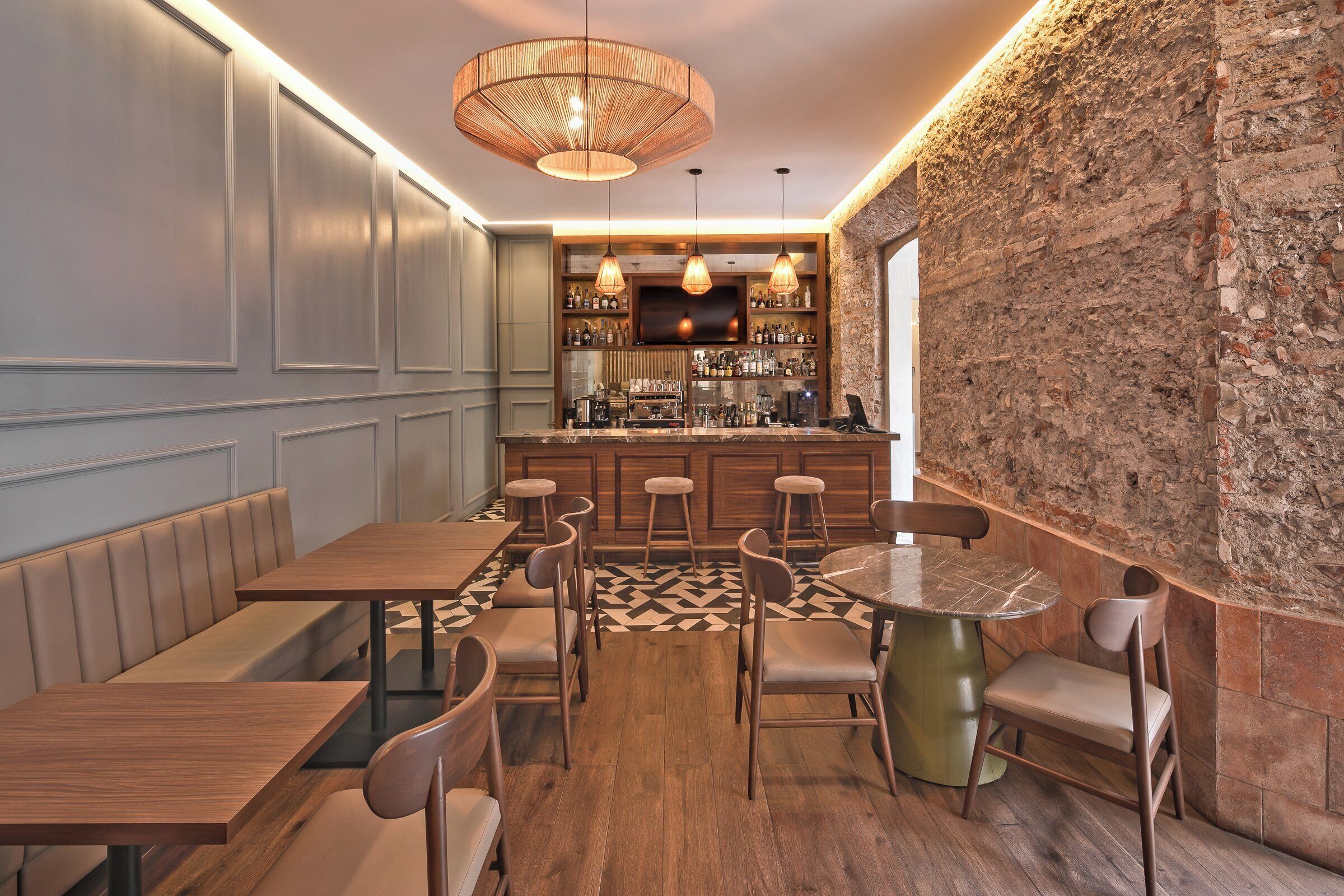 Un restaurante con mesas y sillas de madera, una zona de bar con estantes llenos de botellas y una pared de ladrillo.