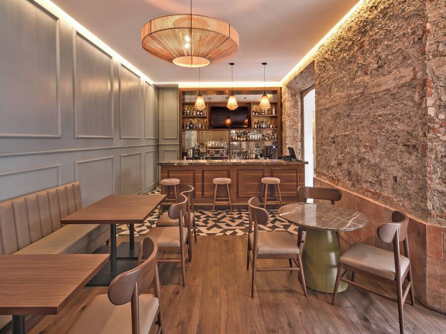 Un restaurante con mesas y sillas de madera, una zona de bar con estantes llenos de botellas y una pared de ladrillo.