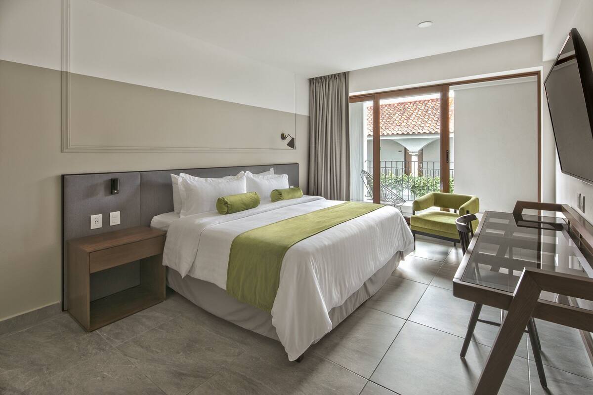 A hotel room with a bed, bedside table, chair, and a TV.