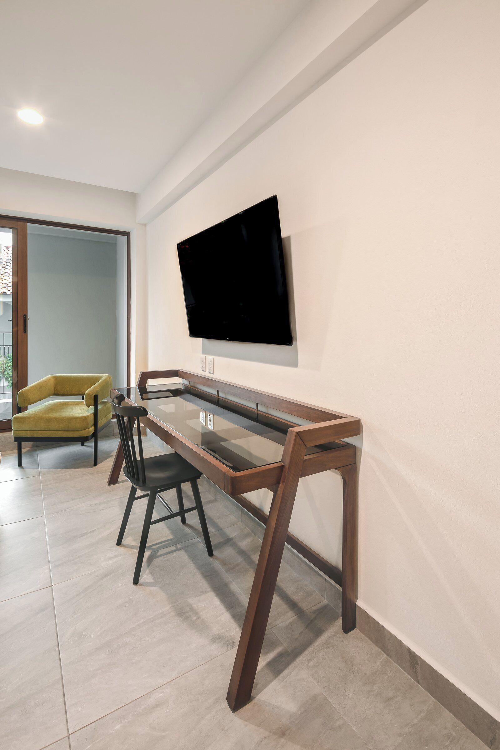 Una sala de estar moderna con una mesa de centro de vidrio, un sillón amarillo y un televisor de pantalla plana montado en la pared.
