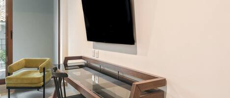 Una sala de estar moderna con una mesa de centro de vidrio, un sillón amarillo y un televisor de pantalla plana montado en la pared.