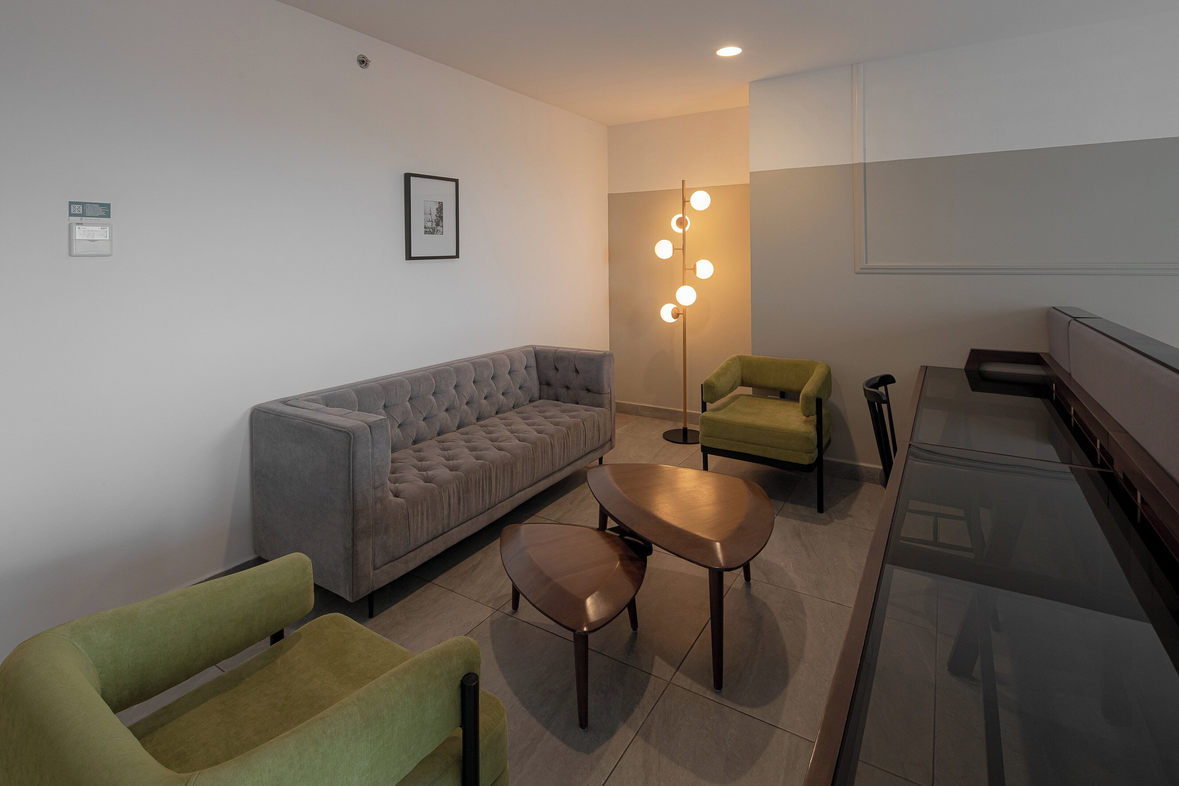 A modern living room with a grey sofa, two green armchairs, a coffee table, and a floor lamp with multiple lights.
