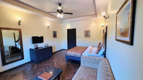 A hotel room with a bed, a sofa, a desk, a television, and a ceiling fan.