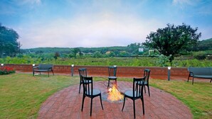 Un patio exterior con un hogar para fuego y sillas, rodeado por un muro de ladrillo, con vistas a un paisaje verde.
