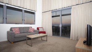A living room with a grey sofa, red and white cushions, a wooden coffee table, a red chair, a TV on a wooden stand, and a sliding glass door leading to an outdoor area. - Central Islington (Townsville)