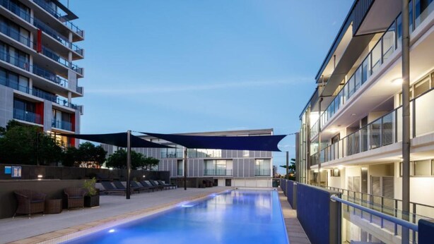 A modern pool area with lounge chairs and a canopy, surrounded by high-rise buildings. - Central Islington (Townsville)
