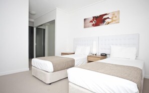 A hotel room with two beds, a bedside table with a lamp, and a painting on the wall.