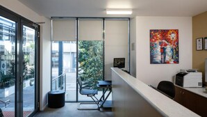 A modern office space with a glass door leading to an outdoor area, a desk with a computer, and a painting on the wall. - Central Islington (Townsville)