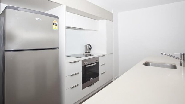A modern kitchen with a stainless steel refrigerator, built-in oven, and a white countertop. - Central Islington (Townsville)