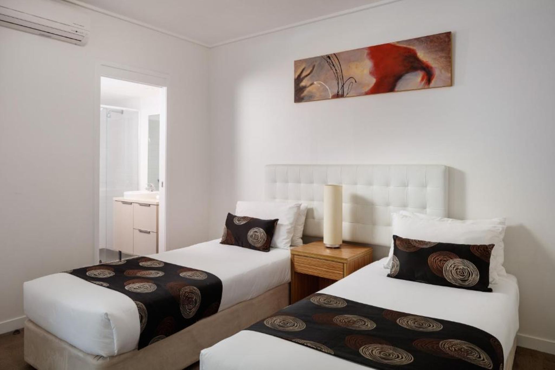 A hotel room with two beds, a nightstand, a lamp, and a painting on the wall.