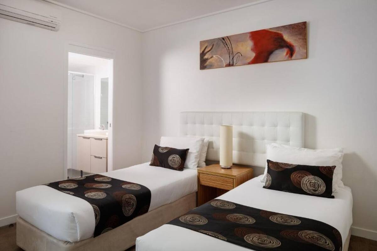 A hotel room with two beds, a nightstand, a lamp, and a painting on the wall.