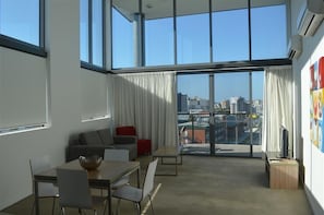 A modern living room with a large window, a sofa, a dining table, and a TV.