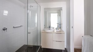 A modern bathroom with a glass shower enclosure, a white sink with a mirror above, and a towel rack. - Central Islington (Townsville)