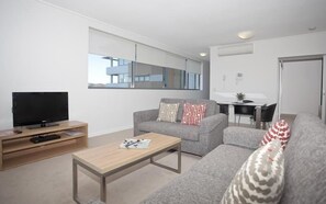 A modern living room with a flat-screen TV, a sofa, a coffee table, and a dining area with a chair and table.