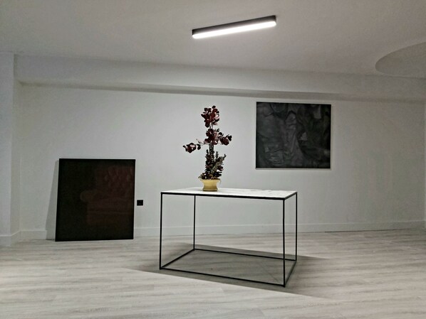 Quarto minimalista com piso de mármore, uma mesa de vidro com planta em vaso e duas obras de arte emolduradas nas paredes.