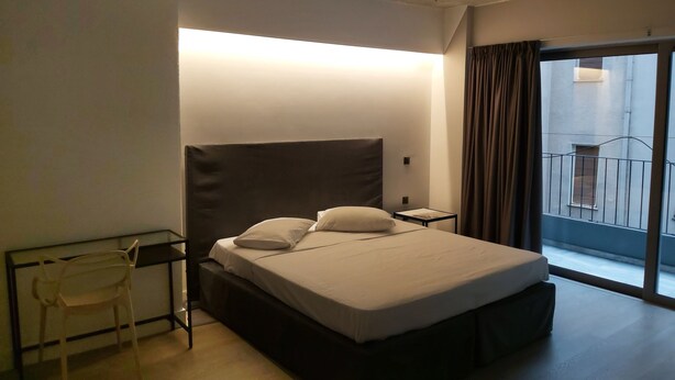 A hotel room with a bed, a chair, a nightstand, and a large window with a view of the outside. - The Link Athens (Athens)