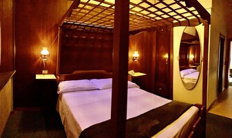Quarto com cama, duas mesas de cabeceira, um espelho e estrutura de teto em madeira.