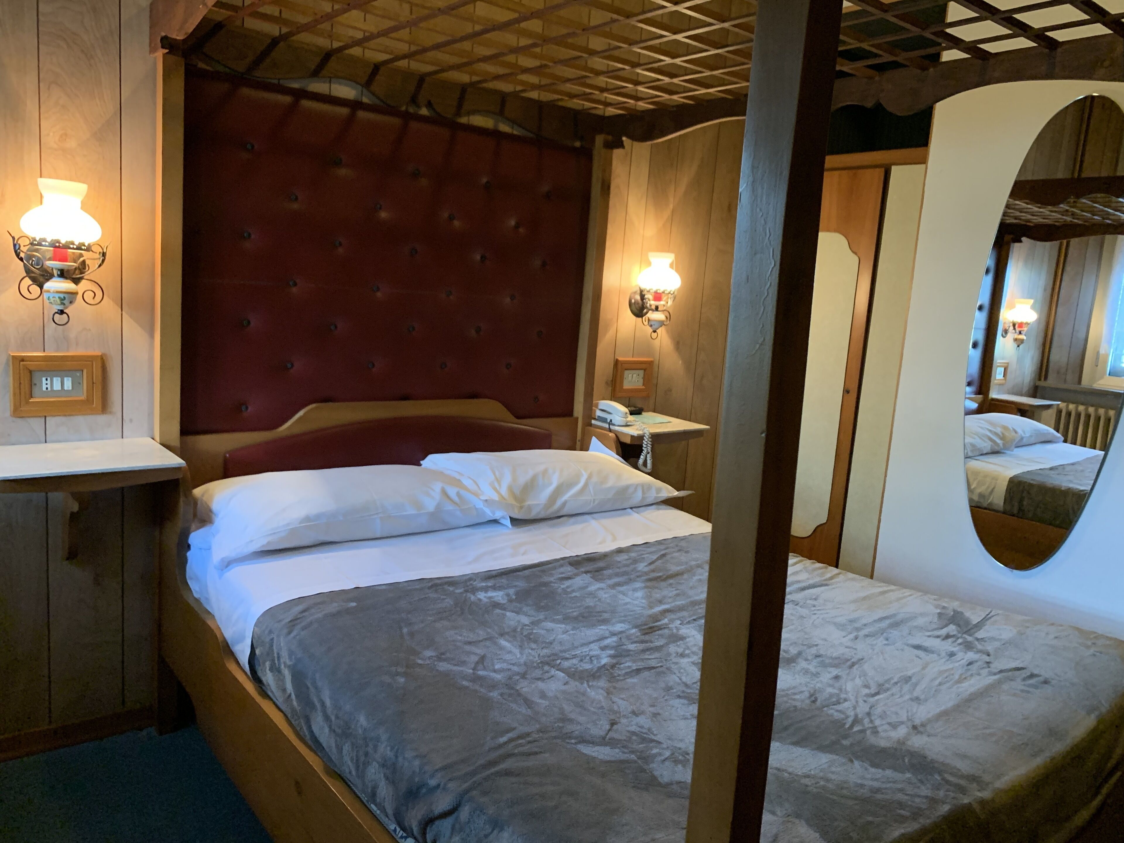 A wooden room with a bed, a mirror, and wall-mounted lights.