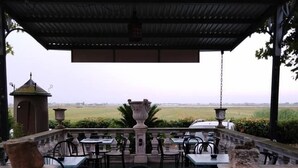 An outdoor seating area with tables and chairs, a view of the countryside, and a small tower structure in the background. - Hotel Ficocle (Cervia)
