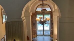 A hallway with an arched doorway leading to a room. There is a chandelier with multiple lampshades hanging from the ceiling. - Hotel Ficocle (Cervia)