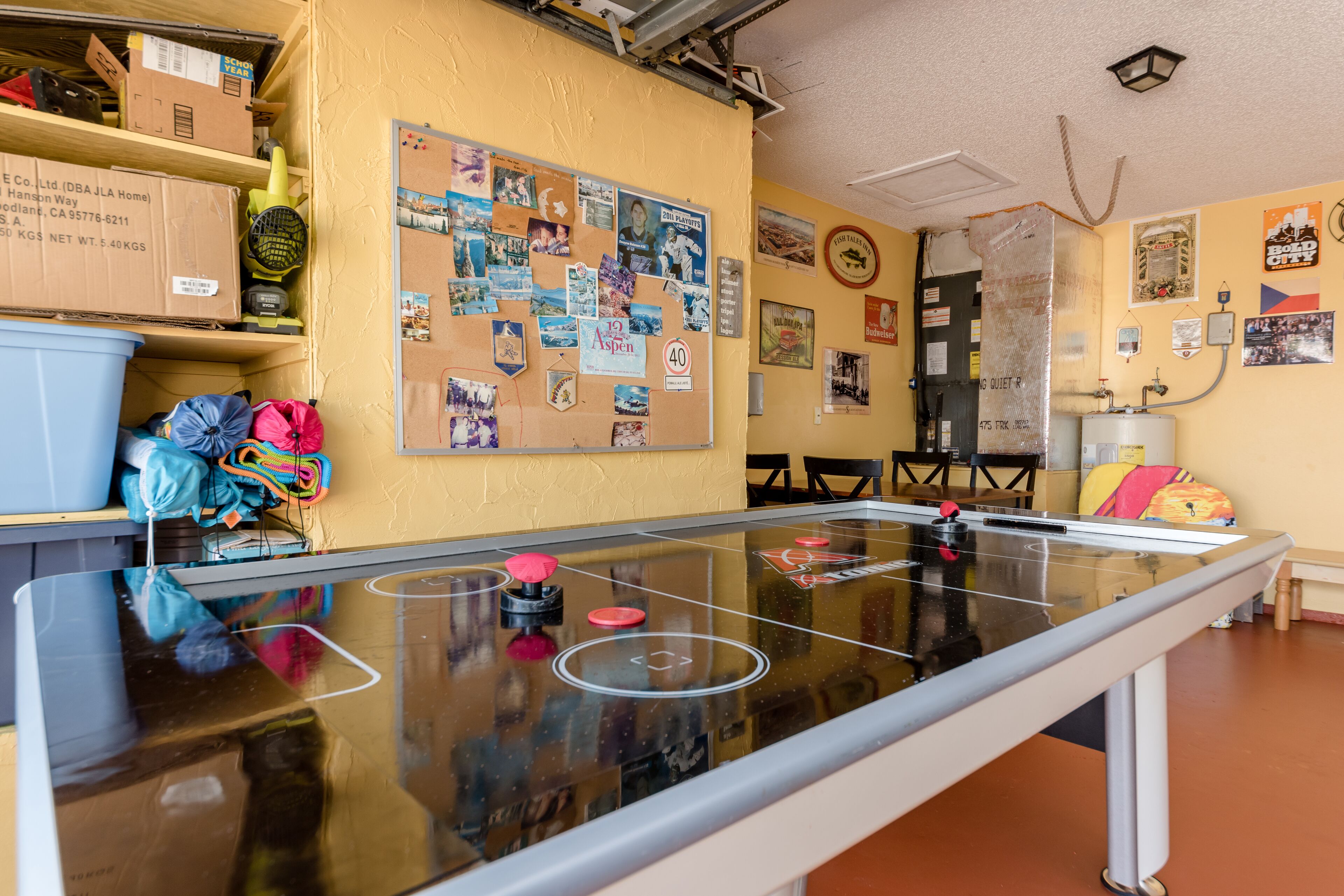 Ein Zimmer mit einem Kicker, einer Pinwand mit verschiedenen Papieren und Fotos sowie einer Tür mit einem Schild.