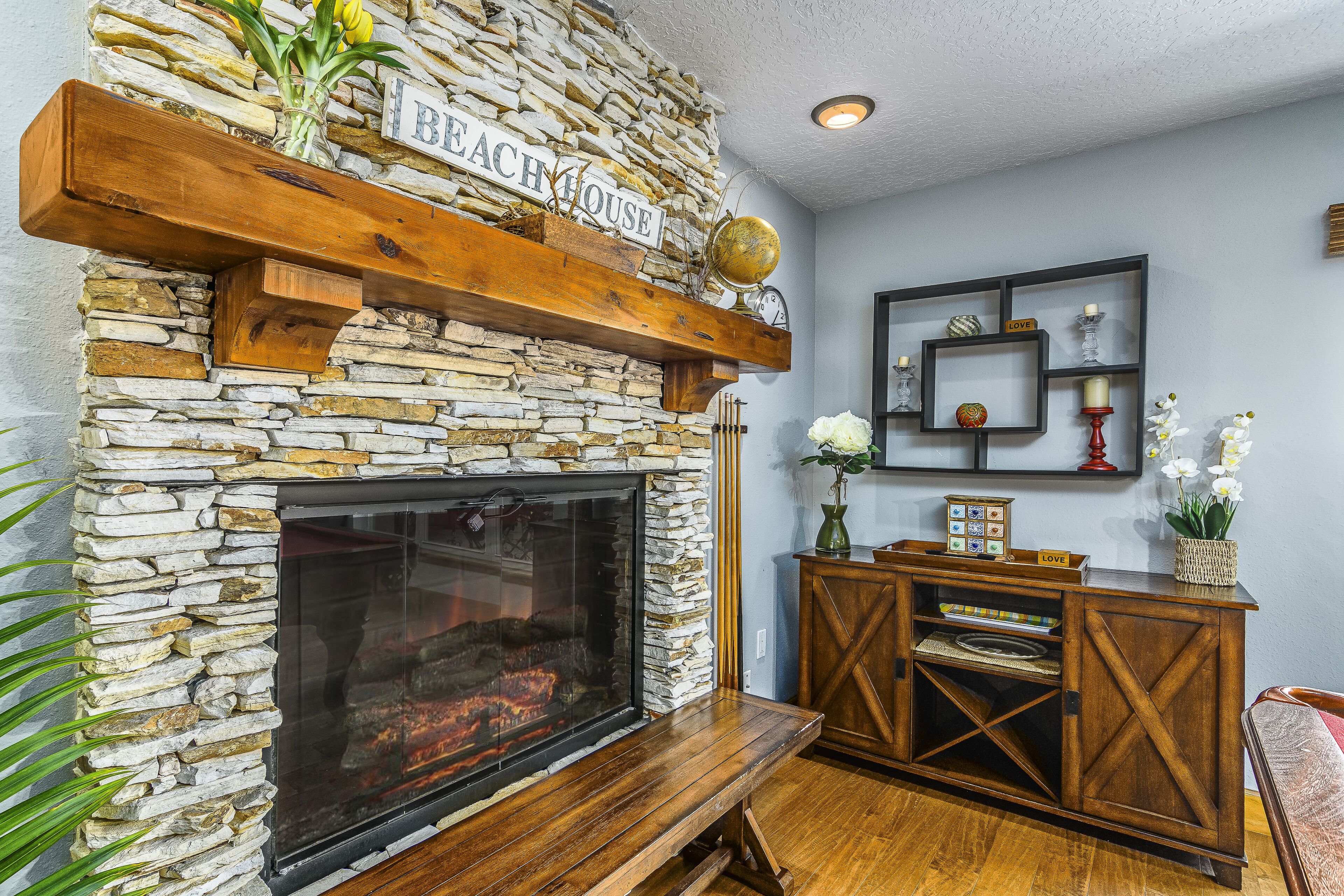 A stone fireplace with a wooden mantel, a bench, and a sign that reads "Beach House".